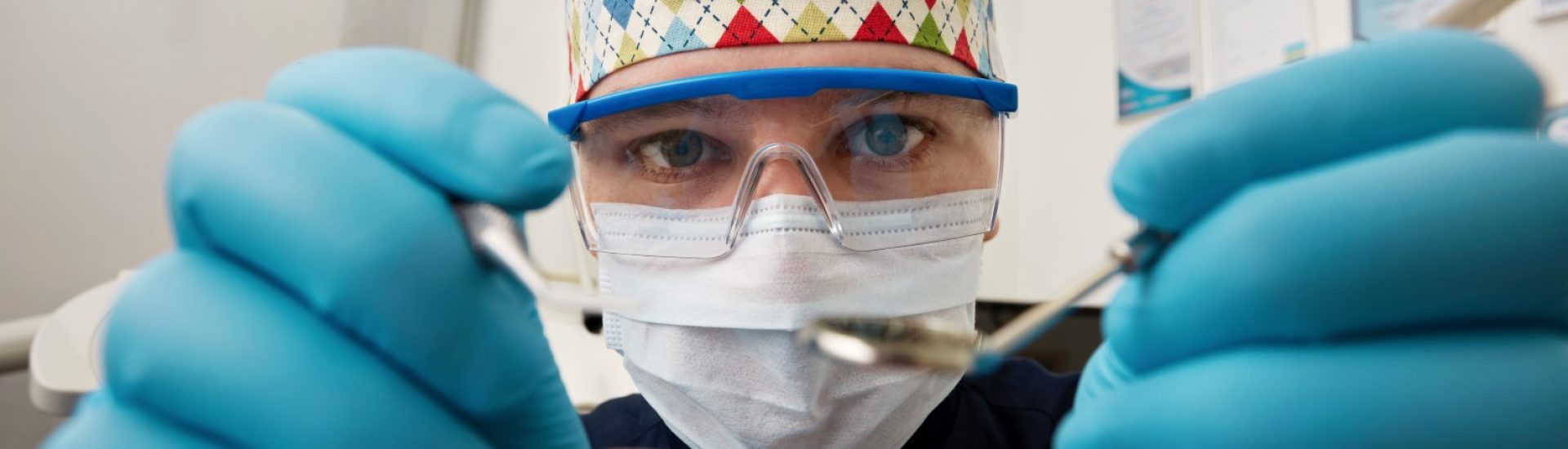 Healthy teeth and smile. Serious doctor directly into the camera. Dentist sitting in the dentist for dental chair and holding a dental drill in hand.